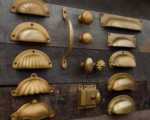 Collection of aged brass cabinet handles and knobs in a Classic finish on a wooden surface