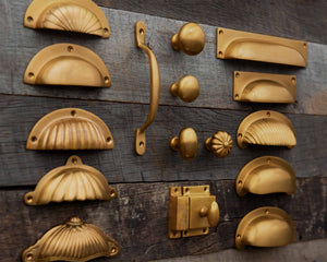 Collection of aged brass cabinet handles and knobs in a Burnished finish on a wooden surface